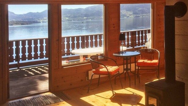 A wooden cabin with a balcony overlooking a lake and mountains. There is a table and two chairs on the balcony. - 8 Person Holiday Home in Etne (Etne)