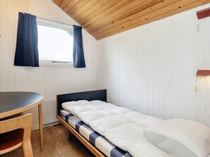 Pieni huone, jossa on yksi sänky, puinen katto, ikkuna verhoilla, yöpöytä ja tuoli.