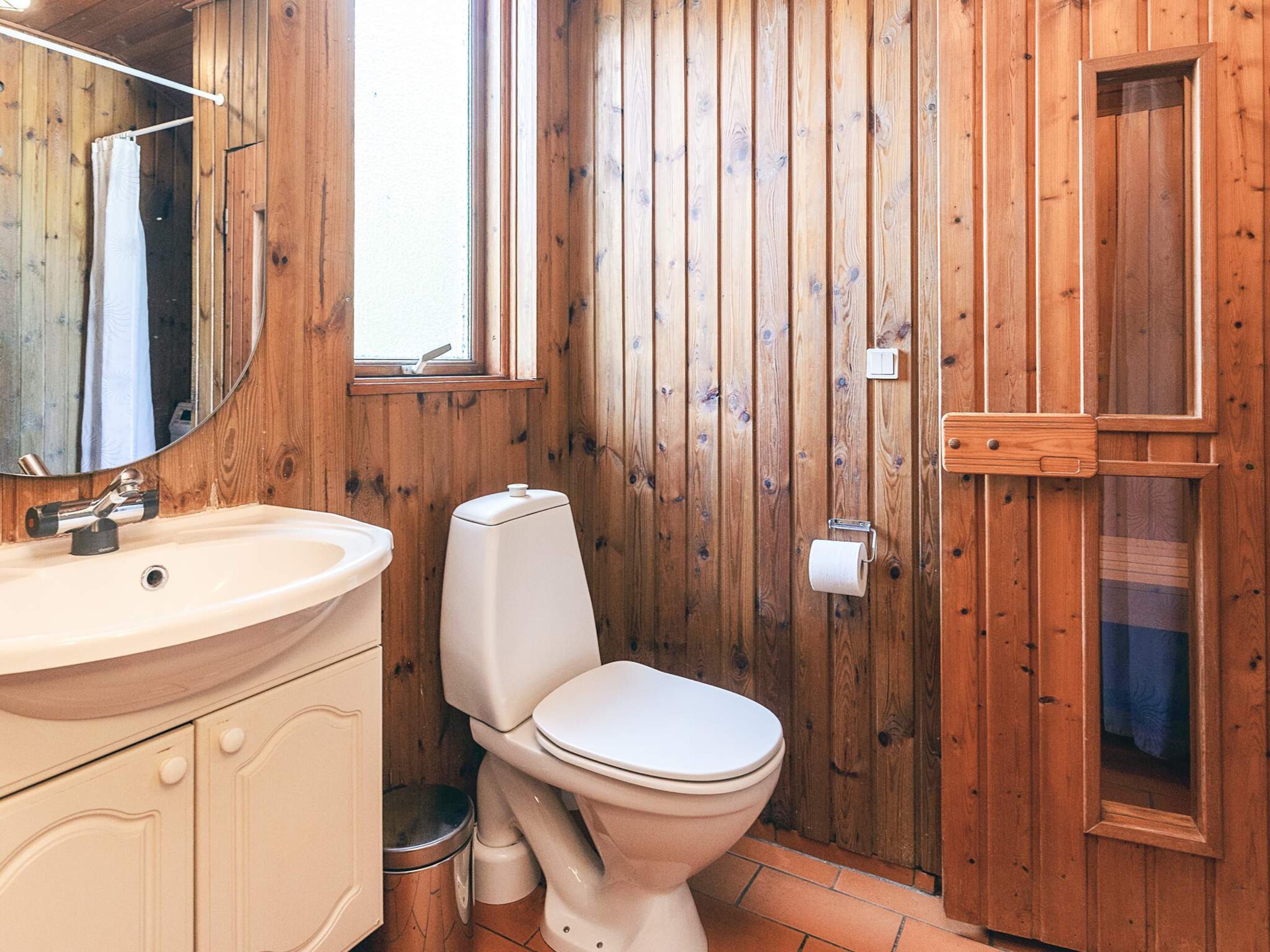 A wooden bathroom with a sink, toilet, and a mirror.