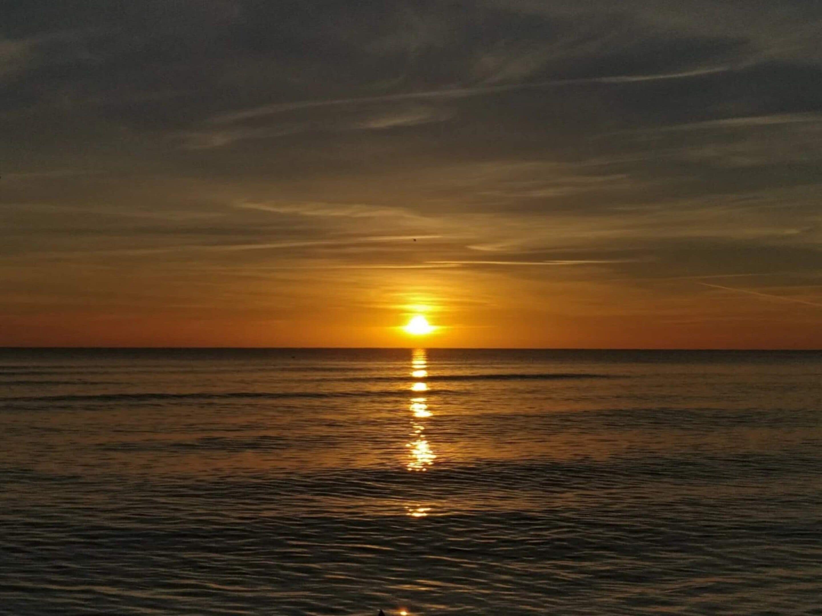 Um pôr do sol sobre um mar calmo, com horizonte límpido.