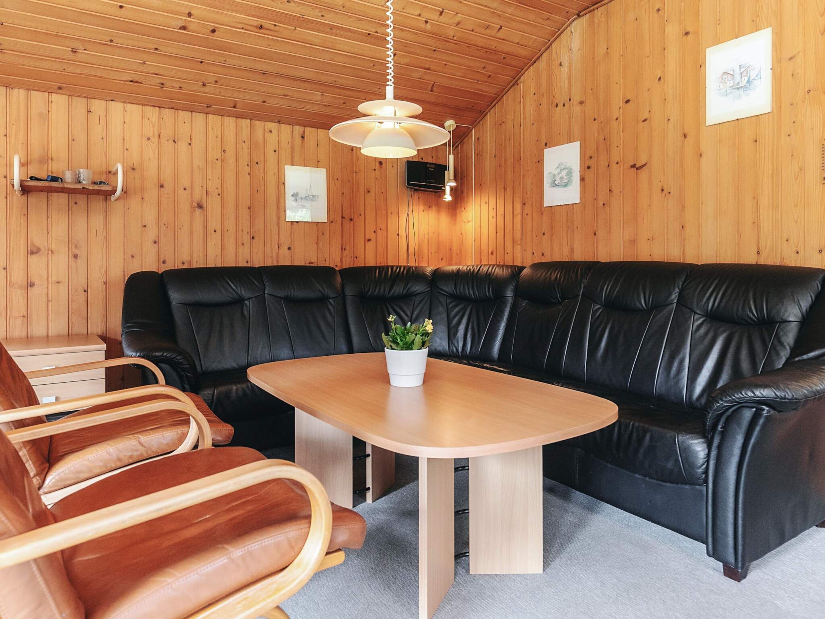 Une pièce chaleureuse avec un canapé en cuir noir, une table en bois ornée d’une plante en pot et un plafond en bois.