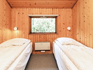 Una habitación pequeña con paneles de madera, dos camas individuales, una ventana con vista a árboles y un calentador fijado a la pared.