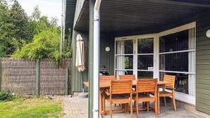 Une terrasse couverte avec une table et des chaises, une clôture en bois et une vue sur la verdure environnante.