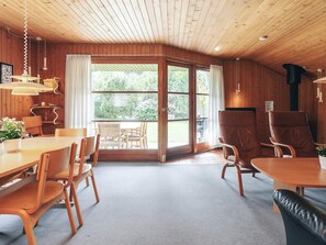 Une pièce aux murs et au plafond en bois, avec une table à manger et des chaises, un canapé et une grande fenêtre avec des rideaux.