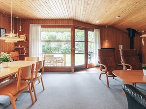 Un interior de madera con zona de comedor, dos sillones de cuero y un ventanal con vistas a la vegetación.