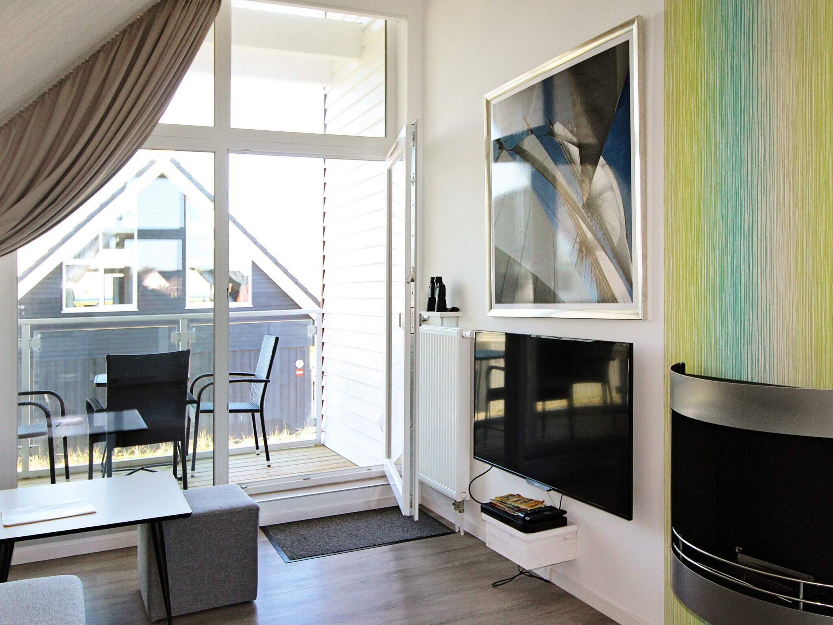 A modern living room with a fireplace, a television, and a large window overlooking a deck.
