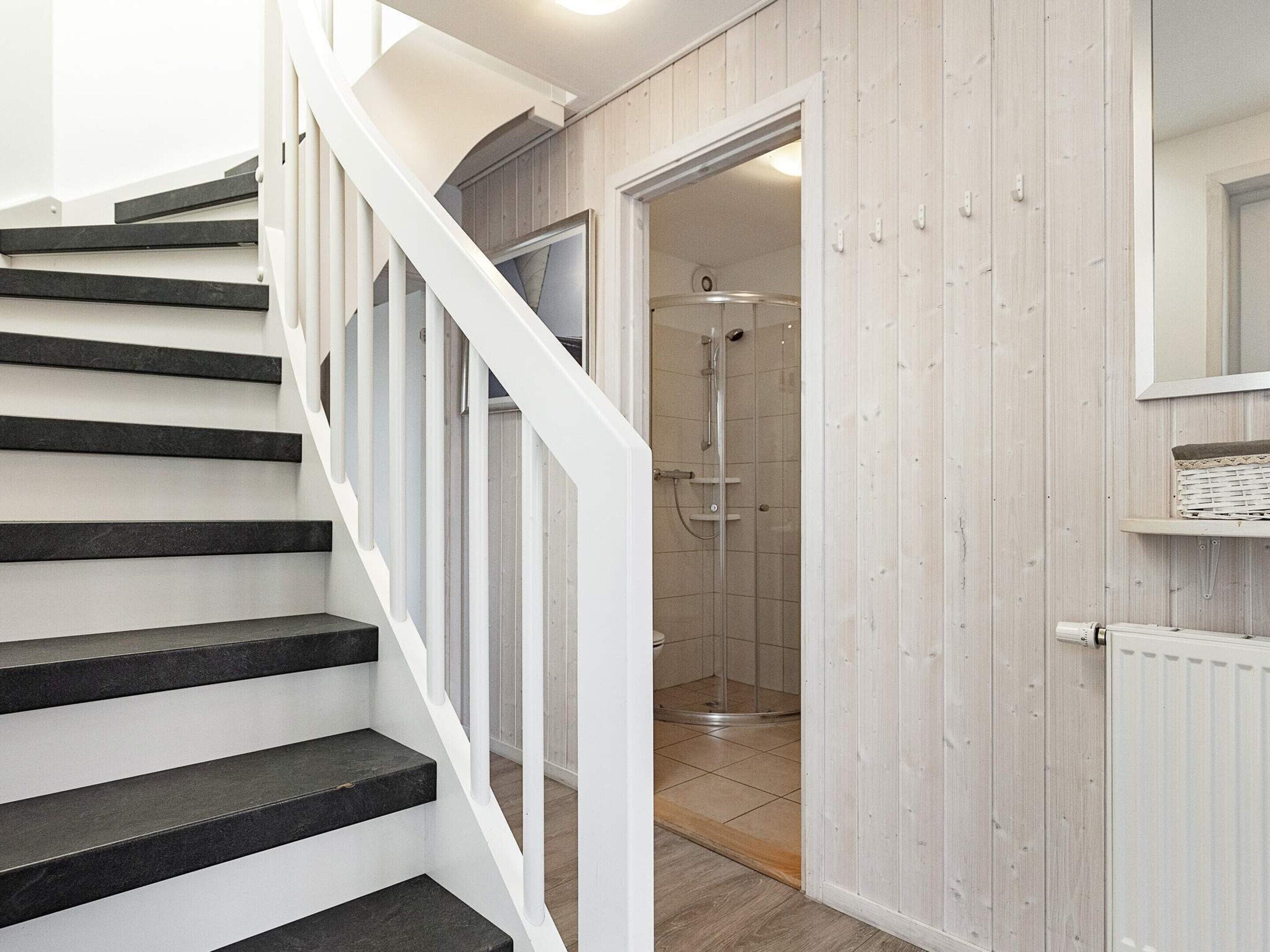 Een trap die leidt naar een douchegedeelte met een houten wand en een witte deur.