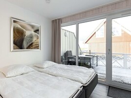 A bedroom with a bed, a framed picture, and a balcony with a table and chairs.