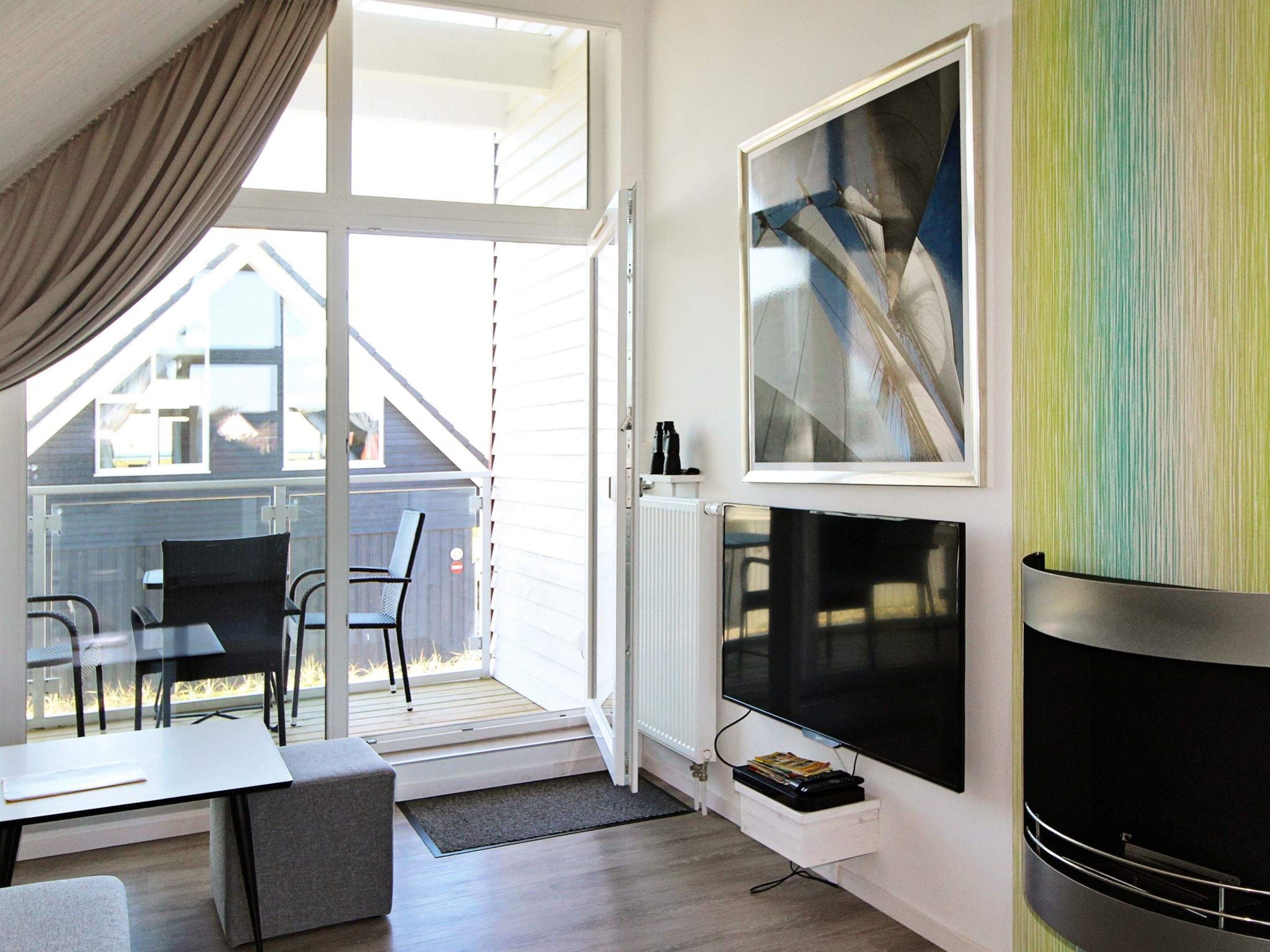 A modern living room with a fireplace, a television, and a large window overlooking a deck.