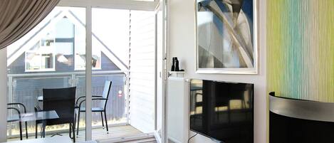 A modern living room with a fireplace, a television, and a large window overlooking a deck.