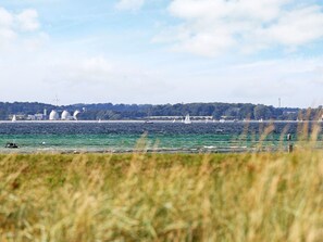 A coastal landscape with a body of water, sailboats, and a distant shoreline with industrial structures. - Holiday Home in Wendtorf (Wendtorf)