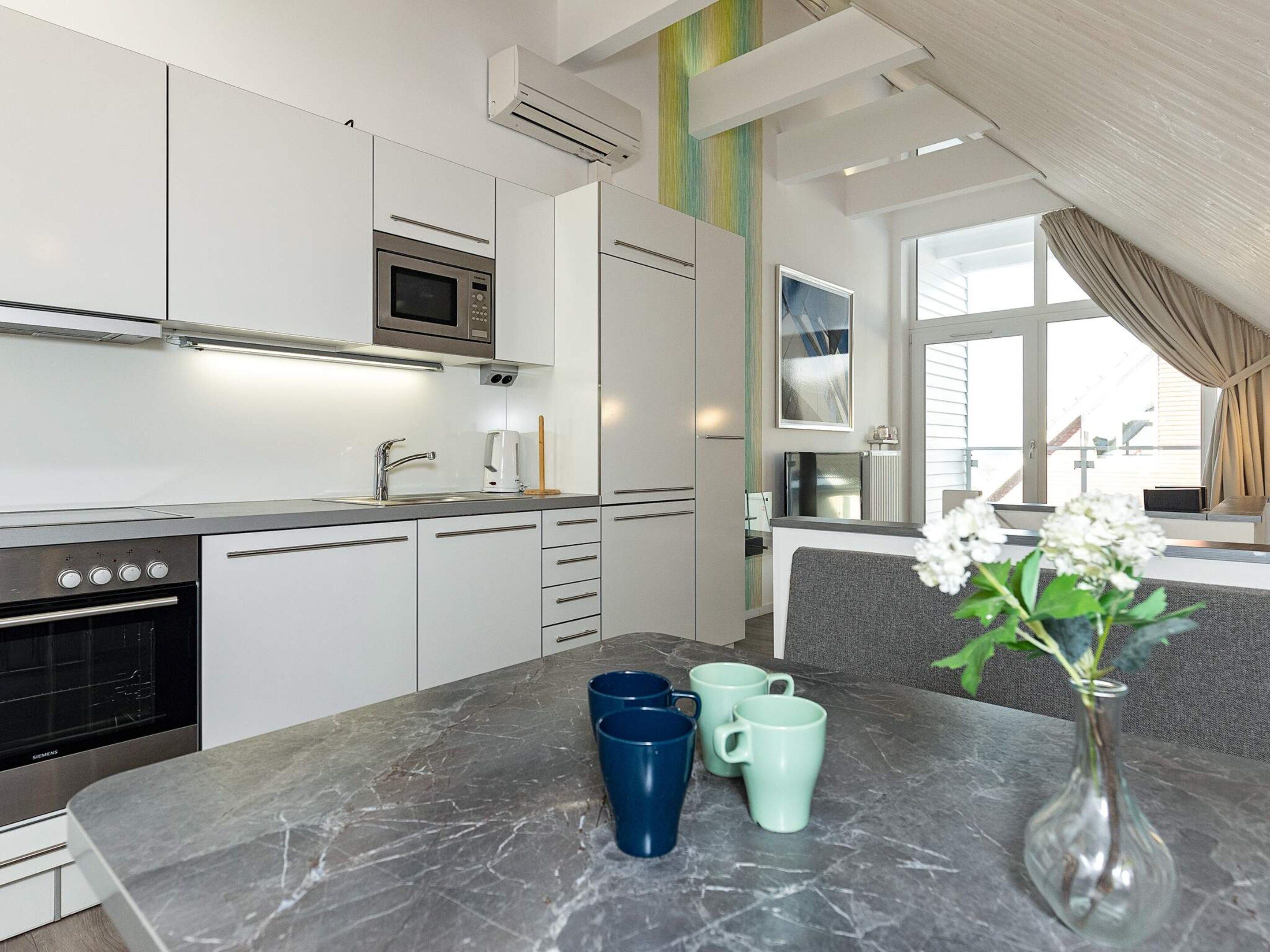 A modern kitchen with white cabinets, a built-in oven, and a marble countertop.