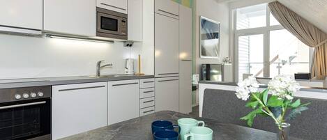 A modern kitchen with white cabinets, a built-in oven, and a marble countertop.