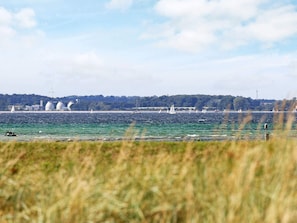 A coastal view with sailboats, a wind turbine, and a distant shoreline with greenery and buildings.