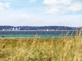 A coastal view with sailboats, a wind turbine, and a distant shoreline with greenery and buildings.
