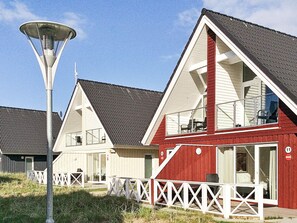 Eine Reihe moderner Strandhäuser in Rot und Weiß mit großen Fenstern und Balkonen, umgeben von einem weißen Zaun und einer Straßenlaterne.