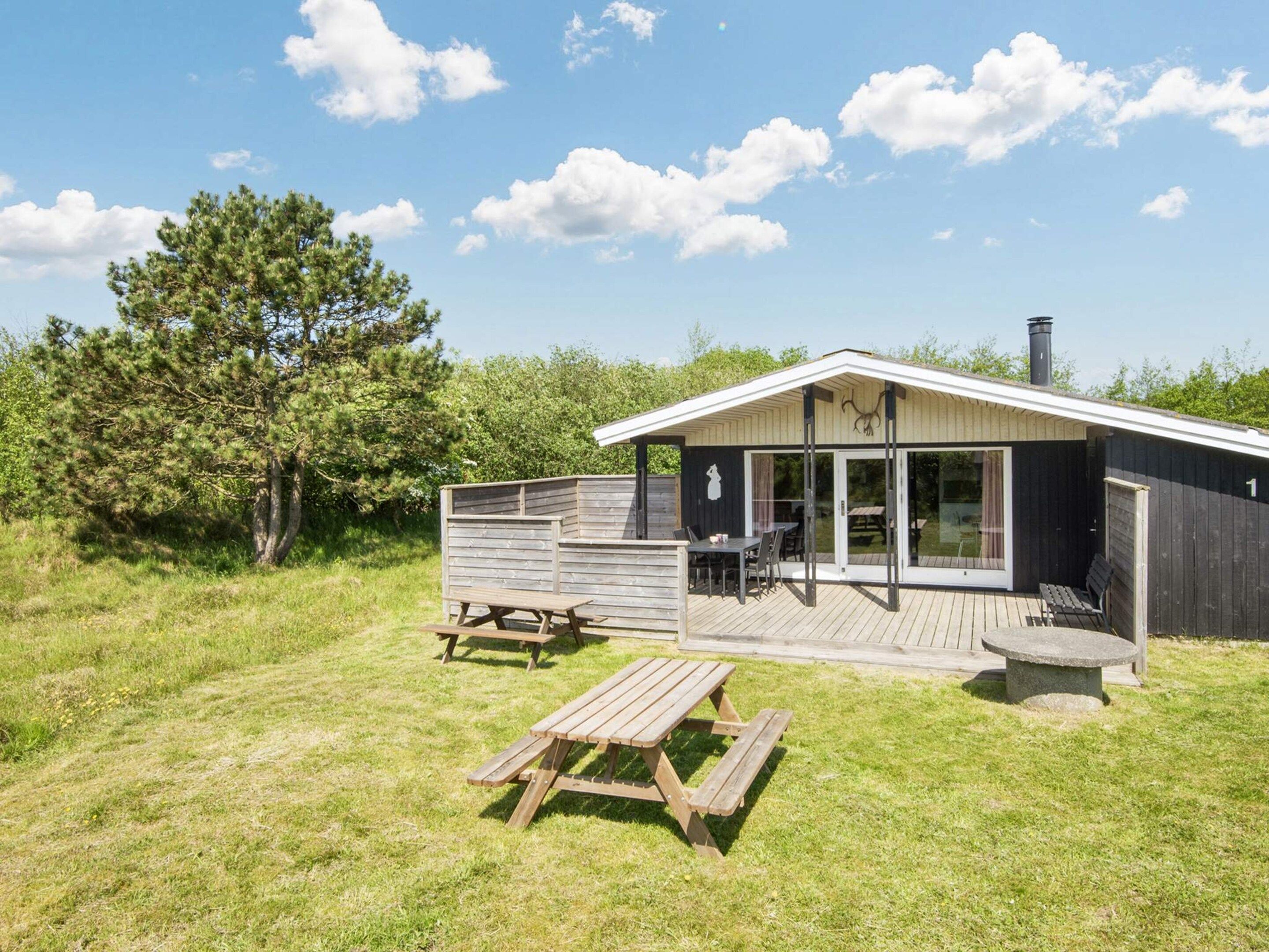 A wooden cabin with a deck, a patio table, and a bench.