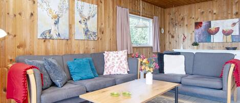 A cozy living room with a grey sofa, a wooden coffee table, and artwork on the walls.