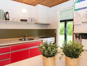 A kitchen with a sink, stove, and red cabinets. There are two woven baskets with plants on the counter. - 6 Person Holiday Home in Fano (Fano)