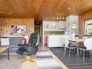 A modern interior with a wooden ceiling, a dining area with white chairs, a black leather sofa, and a kitchen area with white cabinets. - 6 Person Holiday Home in Fano (Fano)