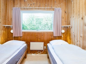 Ein Zimmer mit zwei Betten, einem fensterbelaubten Fenster und einer Wandlampe.