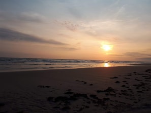 A beach with footprints leading to the water, waves, and a sunset.