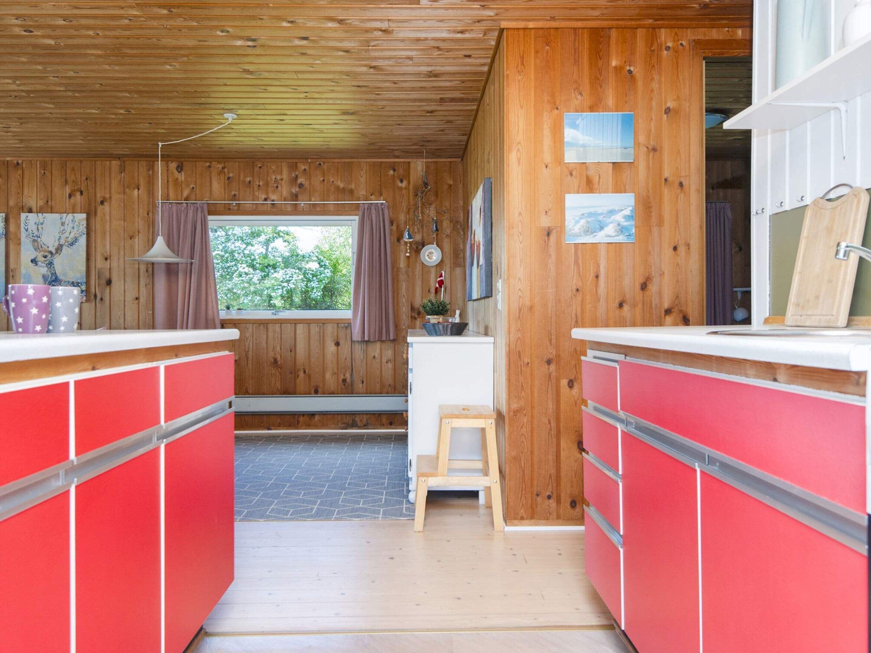 A cabin interior with wooden walls, a kitchenette, and a window with a view of greenery.