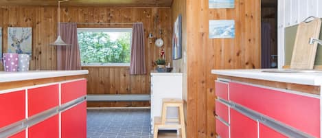 A cabin interior with wooden walls, a kitchenette, and a window with a view of greenery.