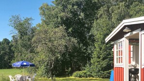 A small red and white building with a porch, surrounded by a grassy yard and dense trees. - 6 Person Holiday Home in Vara (Vara)