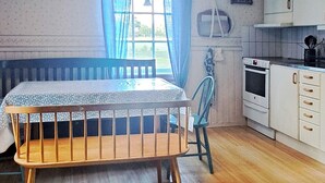 A room with a wooden table, a blue chair, a window with curtains, a kitchen area with cabinets and an oven. - 6 Person Holiday Home in Vara (Vara)