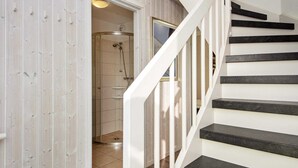 A modern staircase with white railings and dark steps, leading to a room with a wooden wall and a glass shower enclosure. - Holiday Home in Wendtorf (Wendtorf)