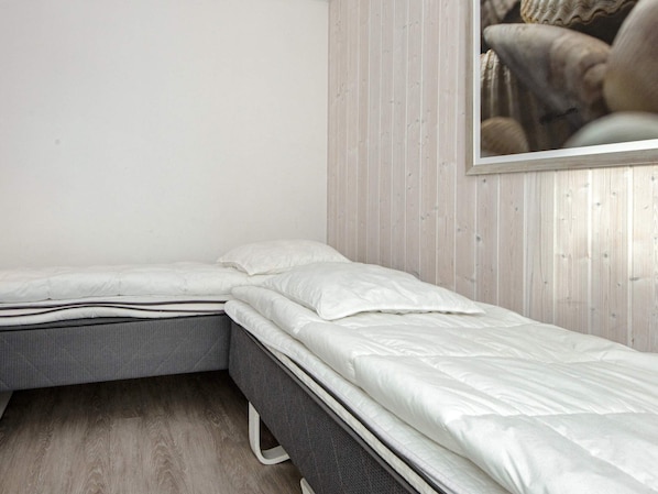A single bed with a grey frame and white bedding in a room with wooden panel walls.