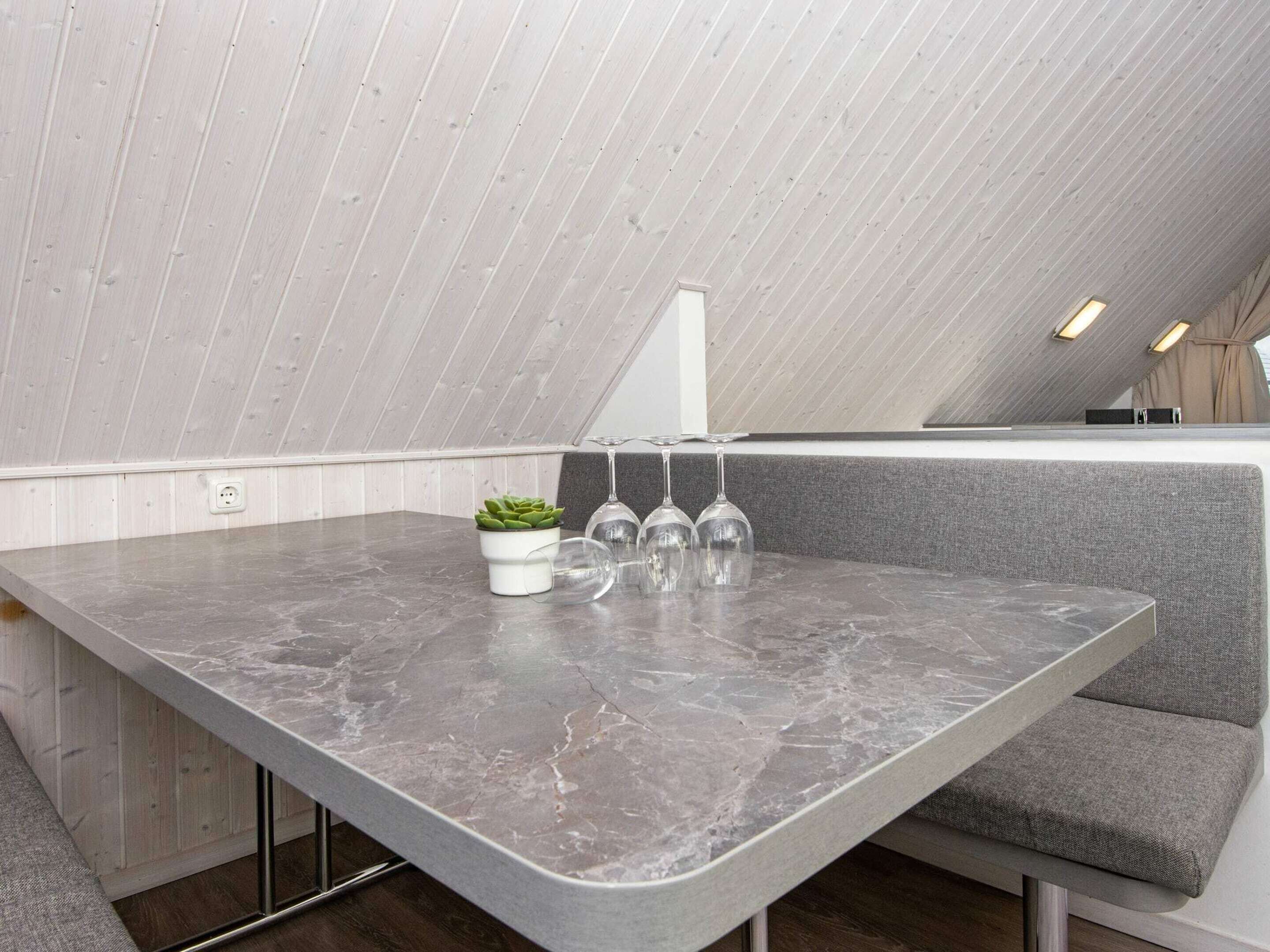A modern kitchen with a marble countertop, a potted plant, and wine glasses.