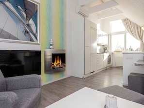 A modern living room with a fireplace, a kitchen with white cabinets, and a dining area with a table and chairs.