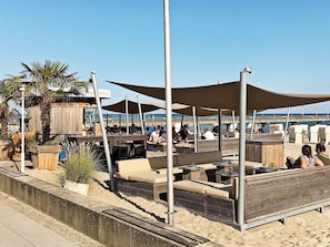 Een restaurant aan het strand met terras, een houten dek en uitzicht op de oceaan.