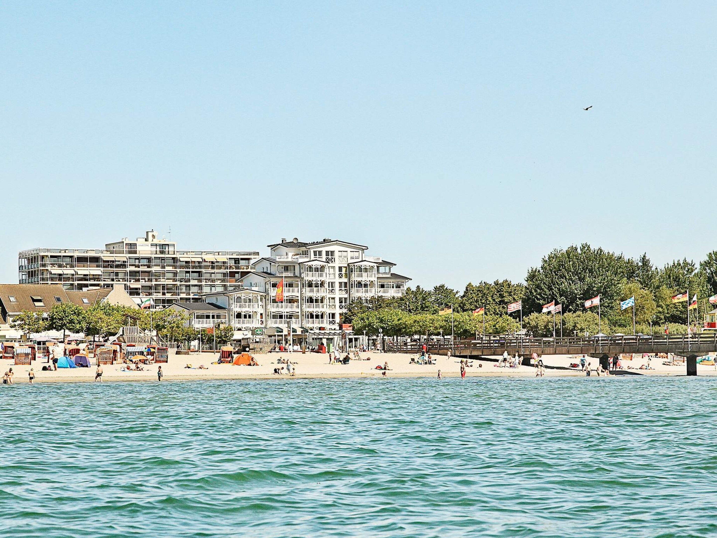 A coastal hotel with multiple floors, a beach in the foreground, and a clear sky.