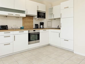 Een moderne keuken met witte kastjes, een magnetron, een koffiezetapparaat en een broodrooster.