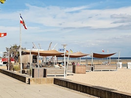 Un paseo marítimo con una fila de sombrillas de playa, una bandera y un letrero que indica los servicios sanitarios.