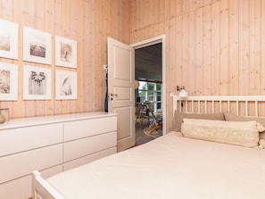A bedroom with a wooden paneled wall, a bed with a white headboard, a dresser, and a door leading to another room. - 4 Star Holiday Home in Oster Assels (Øster Assels)