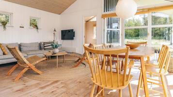 A spacious living area with a wooden floor, a sofa, a coffee table, and a dining table with chairs.