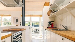A kitchen with white cabinets, a wooden countertop, a stove, and a coffee maker. - 4 Star Holiday Home in Oster Assels (Ă˜ster Assels)