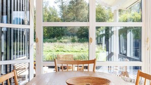A dining area with a wooden table and chairs, large windows offering a view of greenery outside. - 4 Star Holiday Home in Oster Assels (Ă˜ster Assels)