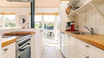 Una cocina con armarios blancos, encimera de madera, estufa y cafetera.