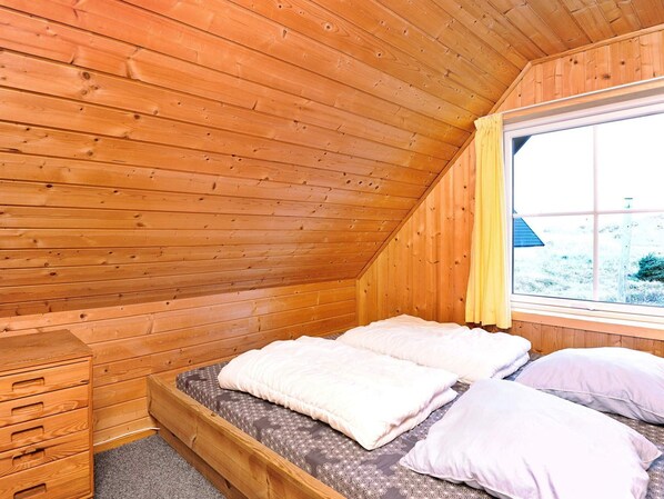 Un dormitorio de cabaña de madera con una cama, un aparador de madera y una ventana con cortina.
