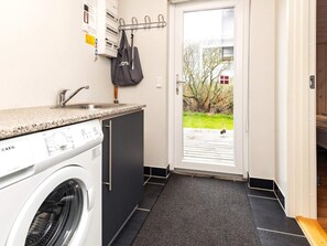 A compact kitchen with a washing machine, a sink, and a door leading to an outdoor area. - 4 Star Holiday Home in Hirtshals (Hirtshals)