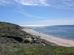 A beach with a grassy hill, a wooden fence, and a clear sky.