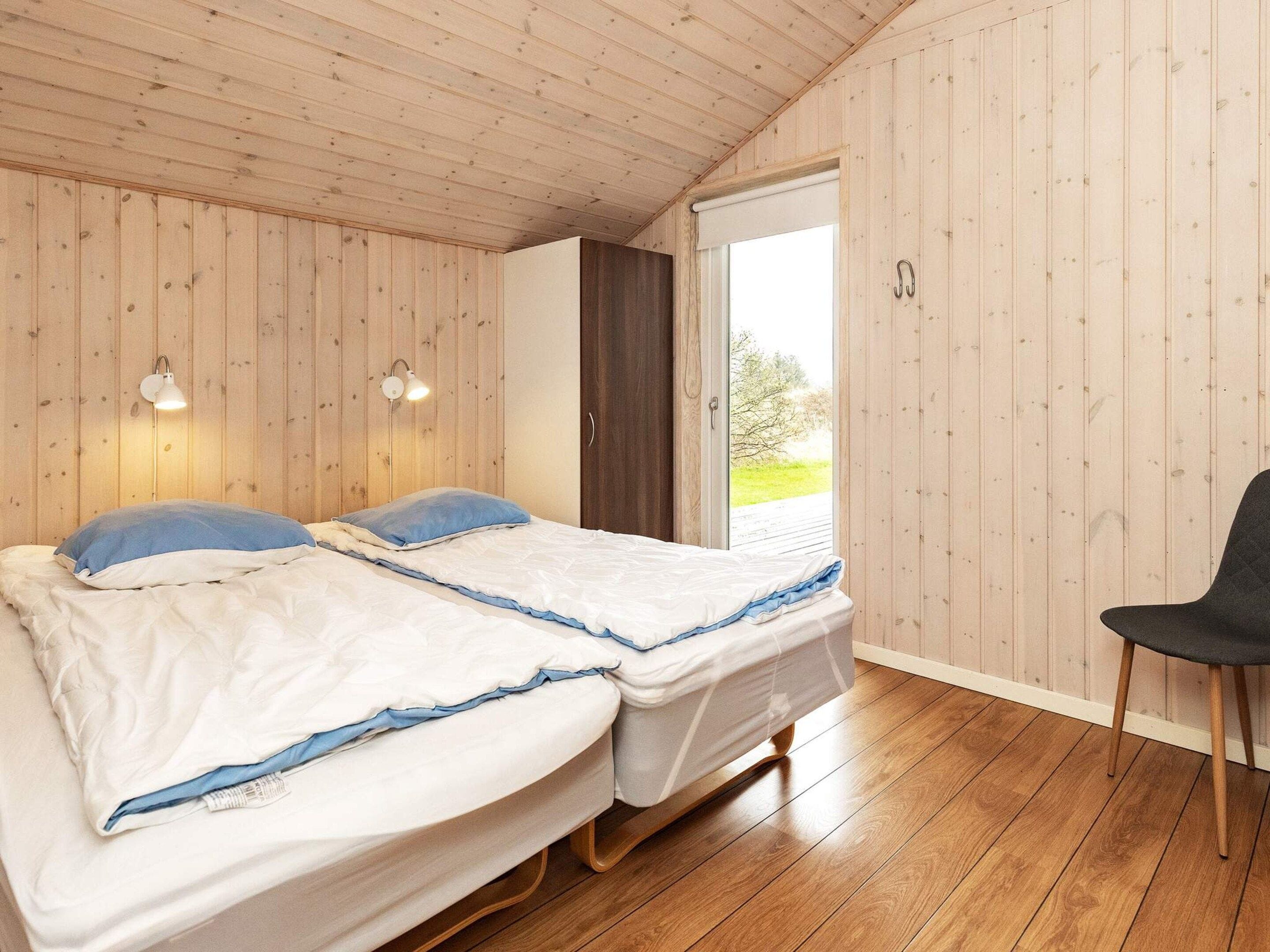 A room with two beds, wooden flooring, a window with a view, and a chair.