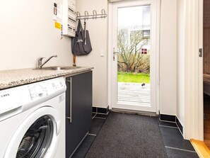 A compact kitchen with a washing machine, a sink, and a door leading to an outdoor area.