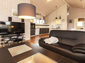 A modern living room with a flat-screen TV, a leather sofa, and a dining area in the background. - 4 Star Holiday Home in Hirtshals (Hirtshals)