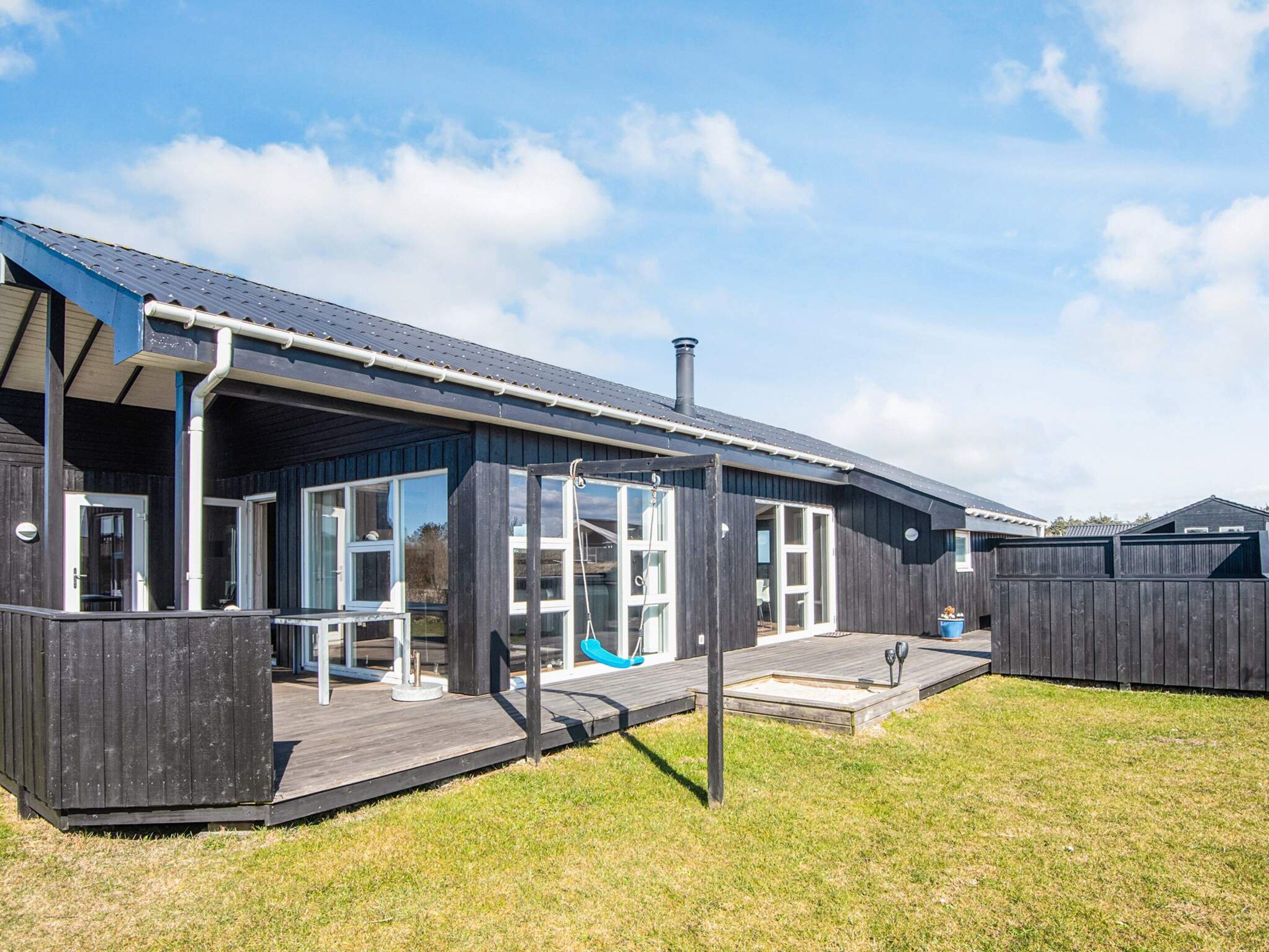 Une maison moderne dotée d’un porche abrité, de grandes fenêtres et d’une cour clôturée.